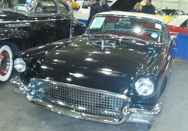 A black 1957 Ford Thunderbird with its wide chrome grille, indoors at a classic car auction